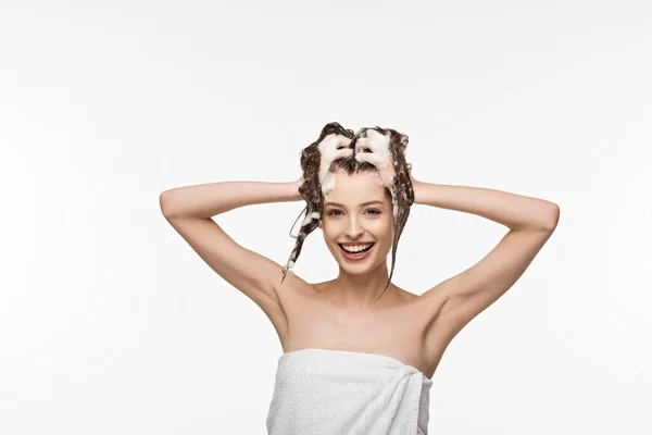 Fille souriante regardant caméra tout en lavant les cheveux isolés sur blanc — Photo de stock