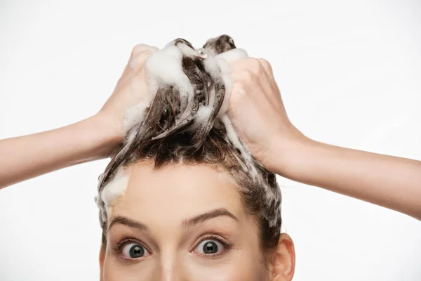 Chica sorprendida con los ojos abiertos lavando el cabello aislado en blanco - foto de stock