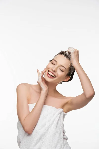 Lächelndes Mädchen, das mit geschlossenen Augen Haare wäscht, während es Gesicht isoliert auf Weiß berührt — Stockfoto