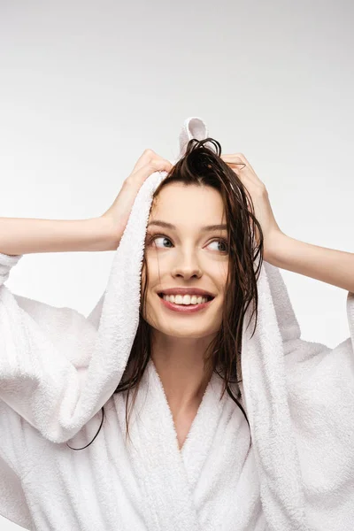 Chica sonriente limpiando el cabello mojado y limpio con toalla blanca mientras mira hacia otro lado aislado en blanco - foto de stock