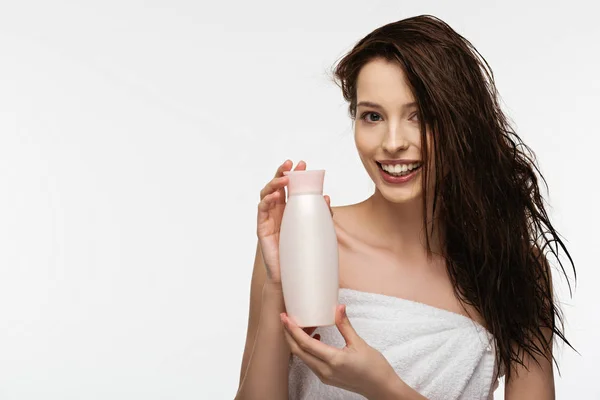 Happy girl looking at camera while holding bottle of shampoo isolated on white — Stock Photo
