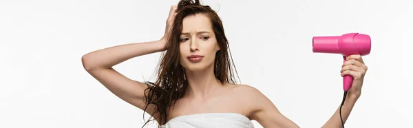 Tiro panorâmico da menina descontente secando o cabelo com secador de cabelo isolado no branco — Fotografia de Stock