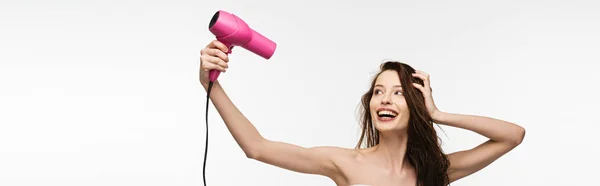 Colpo panoramico di ragazza allegra asciugando i capelli con asciugacapelli isolato su bianco — Foto stock