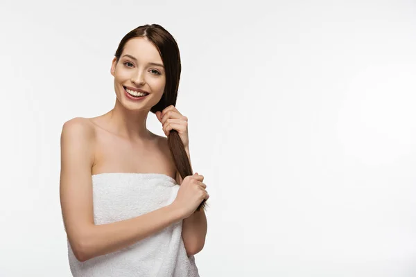 Cheerful girl touching long shiny hair while looking at camera isolated on white — Stock Photo