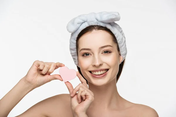 Chica sonriente mostrando en forma de corazón esponja cosmética en la cámara aislada en blanco - foto de stock