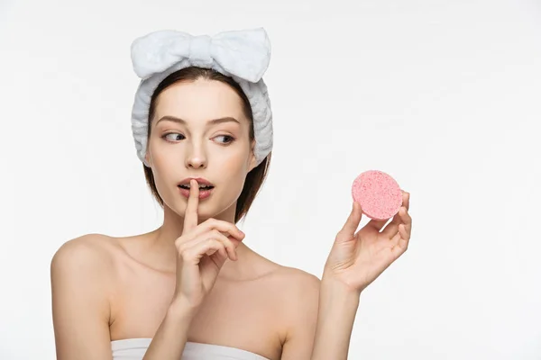 Menina atraente mostrando gesto silencioso enquanto segurando esponja cosmética isolada no branco — Fotografia de Stock