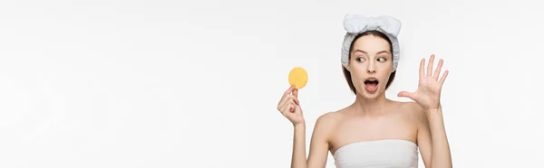 Panoramic shot of surprised girl showing wow gesture while looking at cosmetic sponge isolated on white — Stock Photo