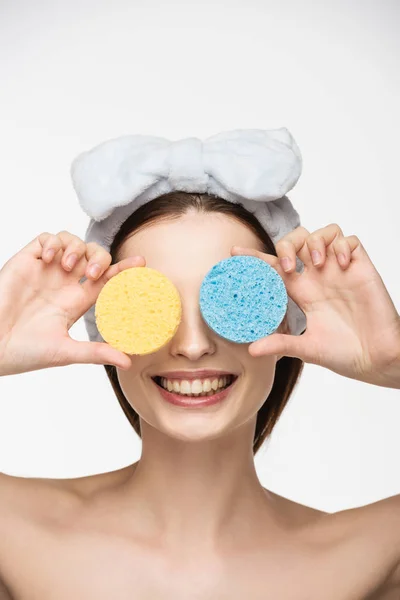 Fille souriante couvrant les yeux avec des éponges cosmétiques colorées isolées sur blanc — Photo de stock