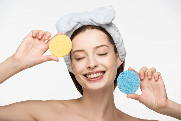 Cheerful girl with closed eyes holding colorful cosmetic sponges isolated on white — Stock Photo
