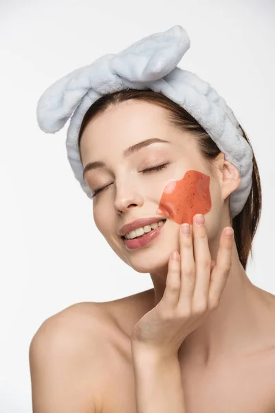 Chica sonriente con los ojos cerrados tocando parche de colágeno en forma de labio en la cara aislada en blanco - foto de stock