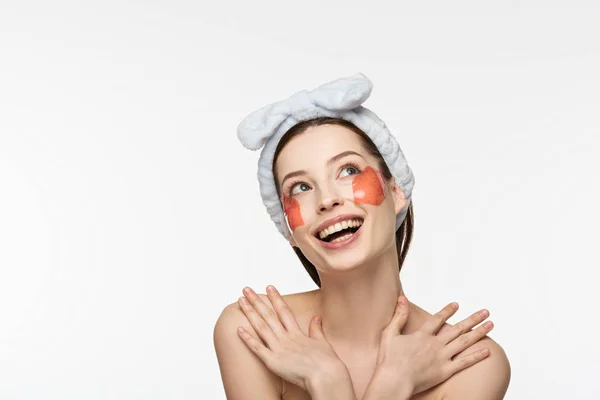 Alegre chica con parches de colágeno en la cara mirando hacia arriba y abrazándose aislada en blanco - foto de stock