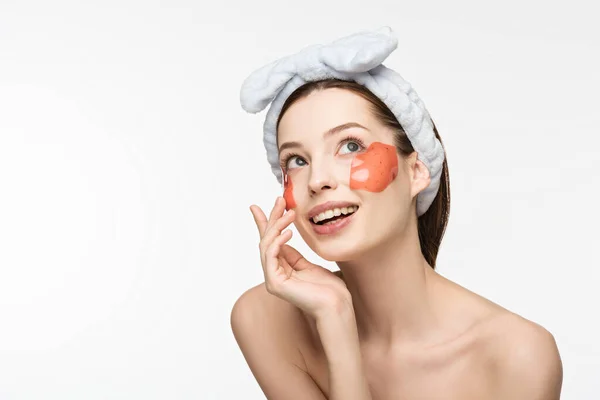 Chica alegre con parches de colágeno en forma de labio tocando la cara y mirando hacia otro lado aislado en blanco - foto de stock