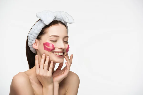 Fröhliches Mädchen mit lippenförmigen Kollagenflecken, die das Gesicht berühren, isoliert auf Weiß — Stockfoto