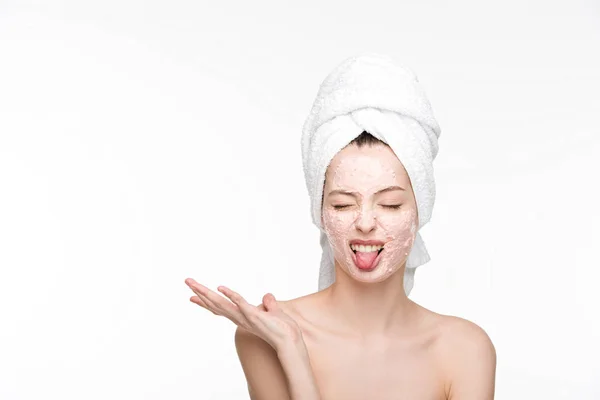 Chica disgustada con mascarilla peladora en la cara que sobresale con la lengua mientras está de pie con el brazo abierto y los ojos cerrados aislados en blanco - foto de stock