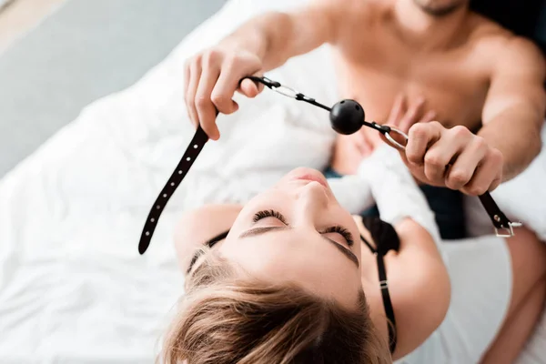 Top view of dominant man holding gag near submissive woman in bedroom — Stock Photo