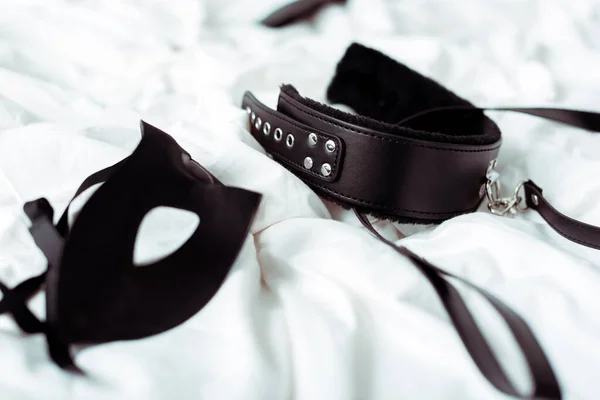 Selective focus of bdsm leash and eye mask on white bedding — Stock Photo