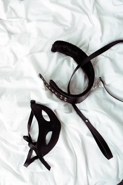 Top view of bdsm leash and eye mask on white bedding — Stock Photo