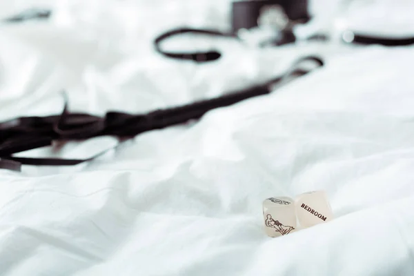 Selective focus of kamasutra dice with bedroom lettering near bdsm leash on white bedding — Stock Photo