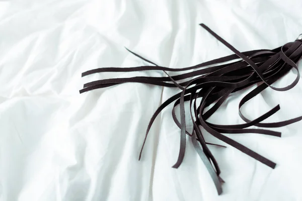 Black leather flogging whip on white bedding — Stock Photo