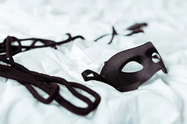 Selective focus of eye mask and black rope on white bedding — Stock Photo