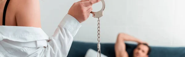 Panoramic shot of woman in shirt holding handcuffs near submissive man — Stock Photo