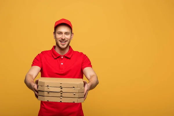 Homem de entrega feliz em uniforme vermelho dando caixas de pizza isoladas no amarelo — Fotografia de Stock