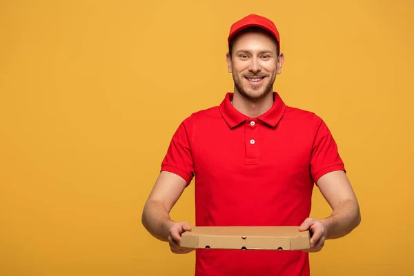 Felice uomo di consegna in uniforme rossa con scatola di pizza isolato su giallo — Foto stock