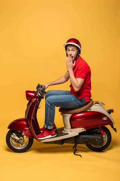 Vue latérale de l'homme de livraison excité sur scooter sur fond jaune — Photo de stock