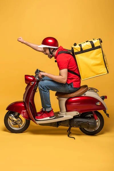 Vista lateral del repartidor con mochila en scooter sobre fondo amarillo - foto de stock