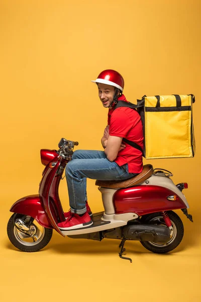 Вид збоку на людину з рюкзаком і схрещеними руками на скутері на жовтому тлі — стокове фото