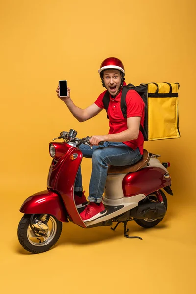 Happy delivery man with backpack on scooter holding smartphone on yellow background — Stock Photo