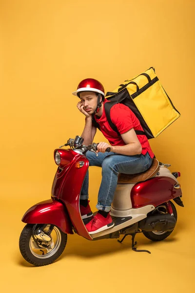 Depressed delivery man with backpack on scooter on yellow background — Stock Photo