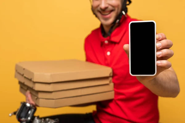 Vista ritagliata di felice uomo di consegna in uniforme rossa contenente scatole di pizza e smartphone con schermo bianco isolato su giallo — Foto stock