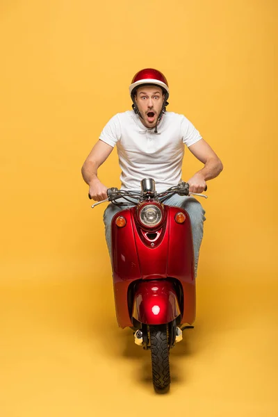Homem de entrega chocado no capacete montando scooter no fundo amarelo — Fotografia de Stock