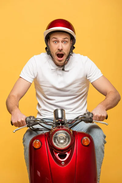 Schockierter Zusteller mit Helm fährt Roller auf gelbem Untergrund — Stockfoto