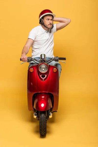 Nachdenklicher Zusteller mit Helm fährt Roller auf gelbem Hintergrund — Stockfoto