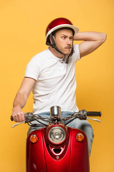 Pensive delivery man in helmet riding scooter isolated on yellow — Stock Photo