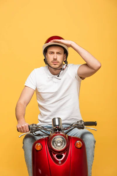 Serious happy delivery man in helmet riding scooter isolated on yellow — Stock Photo