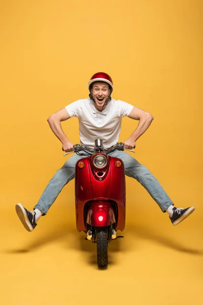 Hombre de entrega feliz en el casco de montar scooter sobre fondo amarillo - foto de stock