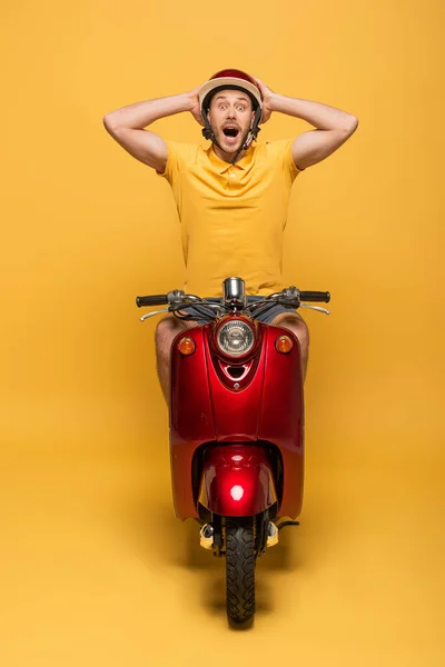 Шокований чоловік доставки в жовтій формі їзди скутер на жовтому фоні — стокове фото