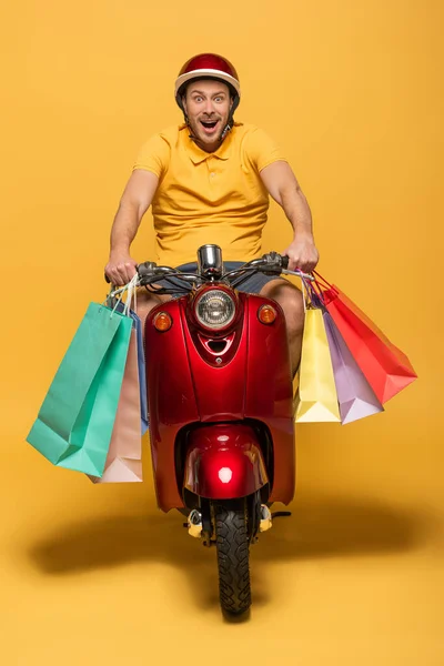 Hombre de entrega feliz en scooter uniforme amarillo con bolsas de compras sobre fondo amarillo - foto de stock