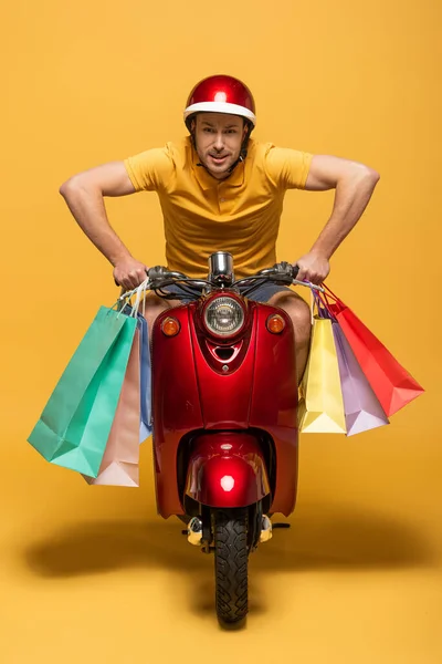 Repartidor en scooter uniforme amarillo con bolsas de compras sobre fondo amarillo - foto de stock