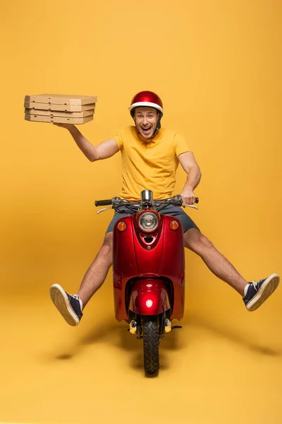 Happy delivery man in yellow uniform riding scooter with pizza boxes on yellow background — Stock Photo