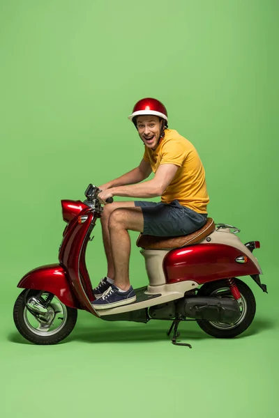 Vista laterale di consegna uomo in uniforme gialla su scooter isolato su verde — Foto stock