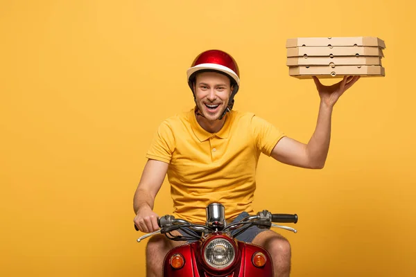 Repartidor sonriente en scooter uniforme amarillo con cajas de pizza aisladas en amarillo - foto de stock