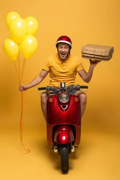 Felice uomo di consegna in monopattino giallo uniforme con scatole di pizza e palloncini su giallo — Foto stock