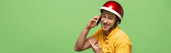 Vista lateral del hombre de la entrega feliz en uniforme amarillo hablando en el teléfono inteligente aislado en verde, tiro panorámico — Stock Photo
