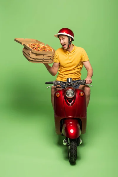 Loco repartidor en uniforme amarillo en scooter entrega pizza en verde - foto de stock