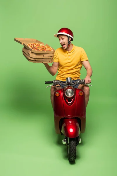 Crazy delivery man in yellow uniform on scooter delivering pizza on green — Stock Photo