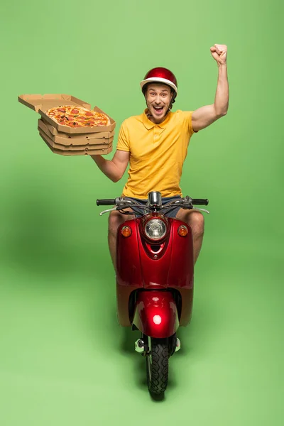 Щасливий чоловік доставки в жовтій формі на скутері, що доставляє піцу і показує так жест на зеленому — стокове фото
